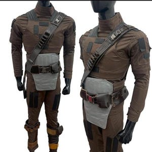 May include: Two brown and grey costumes on mannequins. Each outfit features a high-necked shirt, chest armour, a utility belt, and trousers. The costumes have a tactical design, with multiple pockets and straps.