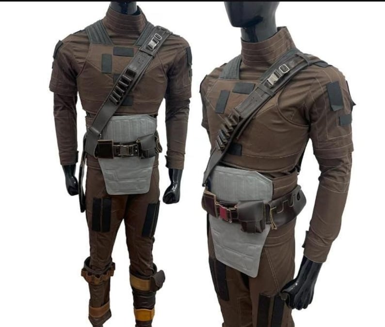 May include: Two brown and grey costumes on mannequins. Each outfit features a high-necked shirt, chest armour, a utility belt, and trousers. The costumes have a tactical design, with multiple pockets and straps.