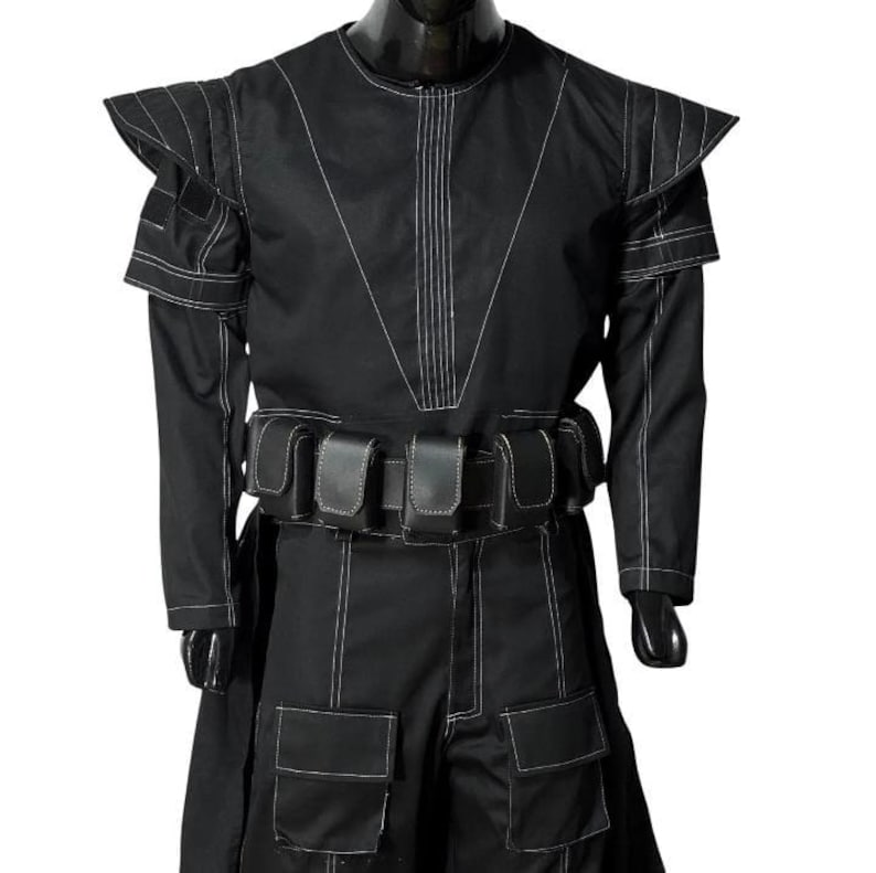May include: Black costume with white stitching details. The outfit features a high collar, shoulder accents, long sleeves, and a belt with pouches. The pants have large pockets. The costume is displayed on a mannequin.