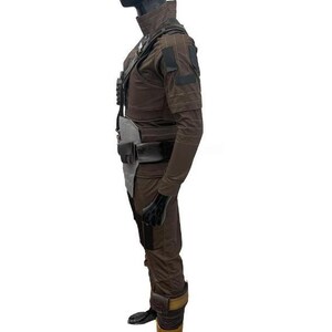 May include: A brown and black costume with a high collar, shoulder pads, and multiple pockets. The outfit includes a belt, pouches, and gloves. The costume is displayed on a mannequin.
