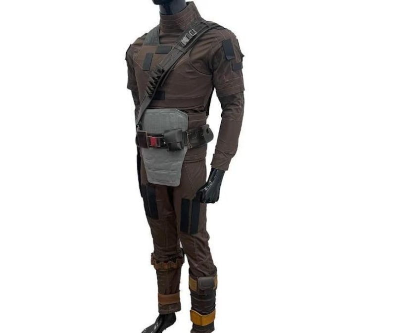 May include: A brown tactical jumpsuit with a chest rig, belt, and shoulder strap. The outfit includes a grey chest plate, black gloves, and brown boots. The mannequin is on a white background.