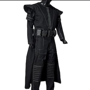 May include: Black costume with white stitching details. The outfit includes a long coat, pants with pockets, and a belt with pouches. The shoulders have a unique design. The costume is displayed on a mannequin.