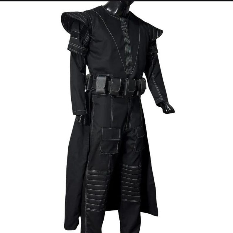May include: Black costume with white stitching details. The outfit includes a long coat, pants with pockets, and a belt with pouches. The shoulders have a unique design. The costume is displayed on a mannequin.
