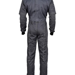 May include: A dark gray racing suit with white stitching details. The one-piece garment features long sleeves with ribbed cuffs, a stand-up collar, and a tailored fit. The suit has a zipper closure and reinforced panels on the shoulders and arms.