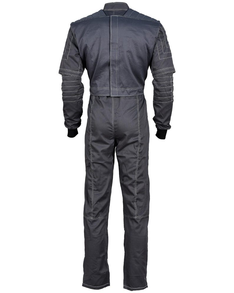 May include: A dark gray racing suit with white stitching details. The one-piece garment features long sleeves with ribbed cuffs, a stand-up collar, and a tailored fit. The suit has a zipper closure and reinforced panels on the shoulders and arms.