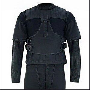Peut inclure: Gilet tactique noir avec manches courtes et col montant. Le gilet pr&eacute;sente une section sup&eacute;rieure rembourr&eacute;e et un panneau central avec deux boucles. Les manches longues ont des coutures verticales. Le gilet est port&eacute; sur une chemise et un pantalon noirs.