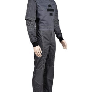 May include: A dark gray jumpsuit with white stitching and black accents. The top has a stand-up collar and a geometric design on the sleeves. The jumpsuit features a two-piece design with a cropped jacket and matching pants.