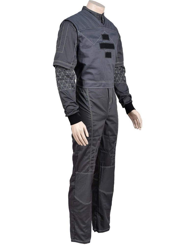 May include: A dark gray jumpsuit with white stitching and black accents. The top has a stand-up collar and a geometric design on the sleeves. The jumpsuit features a two-piece design with a cropped jacket and matching pants.