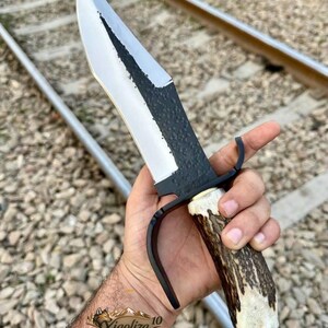 以下が含まれることがあります： 研磨されたスチール製の刃とテクスチャ加工された黒い背を持つ固定刃ナイフ。ハンドルは天然の茶色と白の鹿の角で作られており、黒い金属製のガードとポメルがアクセントになっています。刃にはXiaoliza 10という文字が刻まれています。