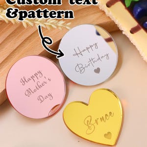 Pode incluir: Três peças decorativas em acrílico: um círculo rosa com "Happy Mother's Day", um círculo prateado com "Happy Birthday" e um coração dourado com "Bruce". A imagem também inclui o texto "Custom text & pattern".