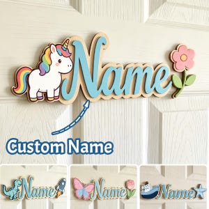 May include: A custom wooden name sign featuring a white unicorn with a rainbow mane and tail, the word Name in light blue script, and a pink flower. Additional examples show a dinosaur, rocket, butterfly, tulip, boat, and starfish designs.