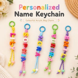 May include: Five personalized name keychains featuring colorful acrylic letter beads strung on braided cords. Each keychain has a circular plastic ring at the top and ends with two small round beads. The names Lily, Sophia, Nora, Aurora, and Emily are displayed.