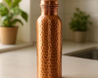 May include: A copper water bottle with a hammered texture. The bottle has a screw-on cap and a cylindrical shape. The copper colour is a warm, reddish-brown. The bottle is approximately 25 cm tall.