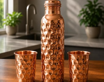 May include: A tall, cylindrical copper water bottle with a textured, hammered surface and a matching screw-top lid, flanked by two smaller, matching hammered copper tumblers, all featuring a polished, reflective metallic finish.