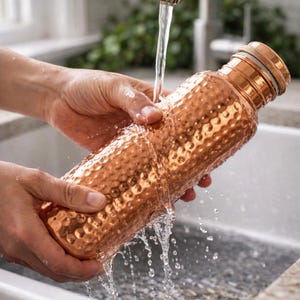 Könnte beinhalten: Eine Kupfer-Wasserflasche mit gehämmertem Muster wird mit Wasser abgespült. Die Flasche hat einen Schraubverschluss und ist zylindrisch geformt. Die Kupferfarbe hat einen warmen, rötlich-braunen Farbton.