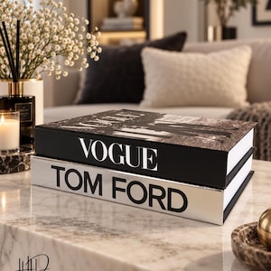 May include: Two rectangular decorative books stacked on a marble surface. The top book is black with the word VOGUE printed in white on the spine and cover. The bottom book is white with the words TOM FORD printed in black on the spine.
