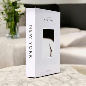 K&ouml;nnte beinhalten: Ein wei&szlig;es Buch mit dem Titel "City Guide New York" mit einem Foto der Freiheitsstatue. Das Buch hat das Wort "Cereal" unten und "New York" vertikal auf dem Buchr&uuml;cken gedruckt.