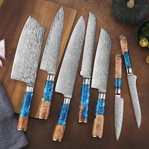 Può includere: Un set di sette coltelli da cucina con lame in acciaio decorate e manici blu e color legno. I coltelli sono disposti su un tagliere di legno, mostrando varie forme di lame per diverse attività culinarie.