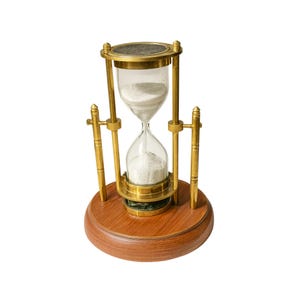 Può includere: Una clessidra con base in legno e struttura in metallo color ottone. La lampadina di vetro contiene sabbia bianca. La clessidra è un oggetto decorativo, utilizzato per misurare il tempo. La base è in legno rotondo e lucido.