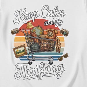 May include: White t-shirt with a graphic of a shopping cart filled with vintage items, including a globe, lamp, and camera. The text "Keep Calm and Go Thrifting" is above and below the cart, set against a sunset background.