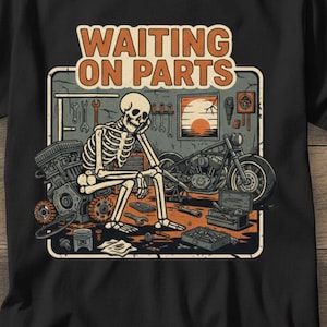 May include: Black t-shirt with a graphic featuring a skeleton sitting in a garage, with a motorcycle and engine parts. The text "WAITING ON PARTS" is displayed above the image in orange letters.