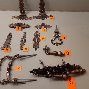 May include: An assortment of antique bronze-toned hardware pieces, including hinges, keyhole covers, drawer pulls, and decorative accents. The collection features ornate designs and various shapes, suitable for furniture restoration or crafting projects.