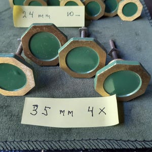 Peut inclure: Une collection de boutons de placard octogonaux dot&eacute;s d'un cadre dor&eacute; m&eacute;tallique et d'un centre circulaire vert mat. Chaque bouton comprend un boulon m&eacute;tallique filet&eacute; &agrave; l'arri&egrave;re. Deux &eacute;tiquettes en papier jaune sont pr&eacute;sentes, marqu&eacute;es 24 mm et 35 mm.