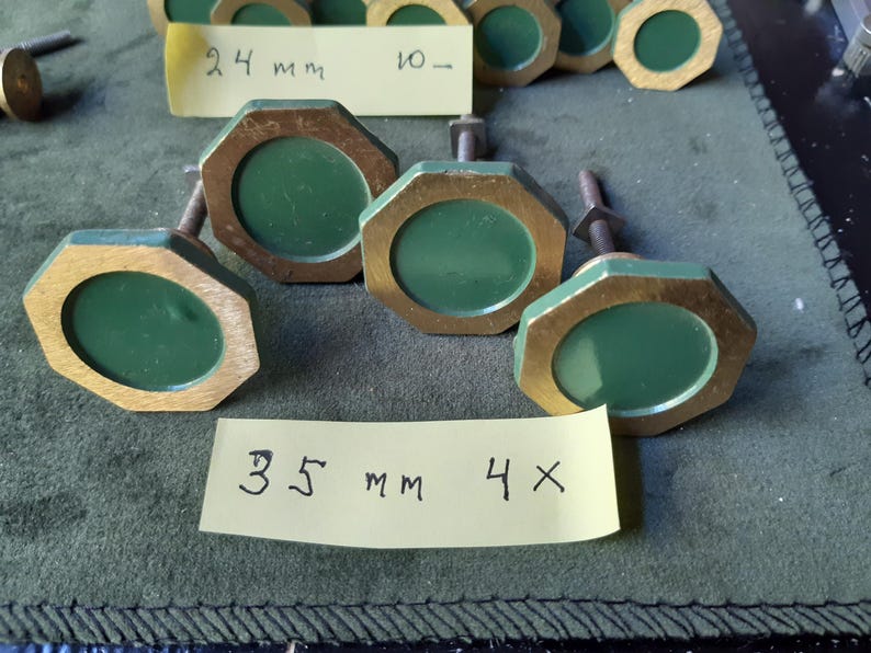 Peut inclure: Une collection de boutons de placard octogonaux dot&eacute;s d'un cadre dor&eacute; m&eacute;tallique et d'un centre circulaire vert mat. Chaque bouton comprend un boulon m&eacute;tallique filet&eacute; &agrave; l'arri&egrave;re. Deux &eacute;tiquettes en papier jaune sont pr&eacute;sentes, marqu&eacute;es 24 mm et 35 mm.