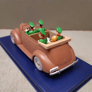 May include: A brown vintage convertible toy car with four figures in green uniforms and hats. The car sits on a blue base. The car has white tires and a license plate that reads "SY-1421".
