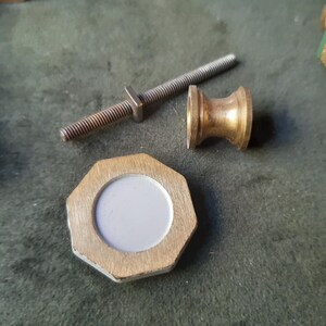 Peut inclure: Un bouton octogonal de couleur laiton avec un centre circulaire gris clair, accompagn&eacute; d'un boulon m&eacute;tallique filet&eacute; s&eacute;par&eacute; et d'une petite pi&egrave;ce d'espacement cylindrique concave de couleur laiton, pr&eacute;sent&eacute;s comme des pi&egrave;ces d&eacute;tach&eacute;es.