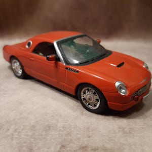 Puede incluir: Modelo a escala de un Ford Thunderbird rojo. El coche en miniatura presenta ruedas plateadas, interior negro y una toma de aire en el capó. El modelo es un objeto de colección.