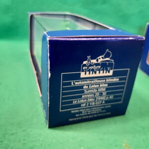 K&ouml;nnte beinhalten: Blaue Box mit Tintin-Logo und franz&ouml;sischem Text. Der Text lautet "L'automitrailleuse blindee du Lotus bleu" und "Sumida ARM ann&eacute;es 20-30". Die Box befindet sich auf einer gr&uuml;nen Oberfl&auml;che.