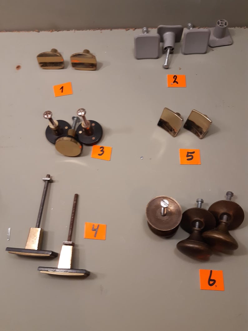 Może przedstawiać: Asortyment okuć do szafek, w tym złote i mosiężne gałki i uchwyty. Kolekcja zawiera r&oacute;żne kształty i rozmiary, w tym kwadratowe, okrągłe i prostokątne wzory. Niekt&oacute;re elementy mają szczotkowane metalowe wykończenie, inne są polerowane.