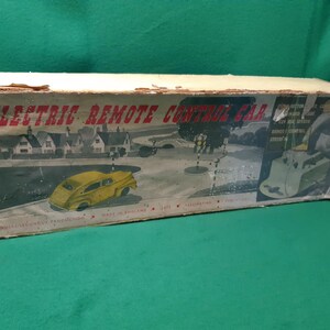 Puede incluir: Caja de juguetes vintage para un coche eléctrico con control remoto. La caja presenta una colorida ilustración de un coche amarillo en una carretera, con el texto "Electric Remote Control Car". Fabricado en Inglaterra.