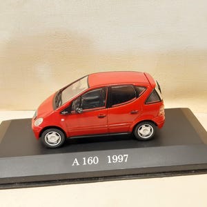 Puede incluir: Modelo a escala rojo de un Mercedes-Benz A 160 de 1997. El coche en miniatura está sobre una base negra. El modelo mide aproximadamente 15 cm de largo.