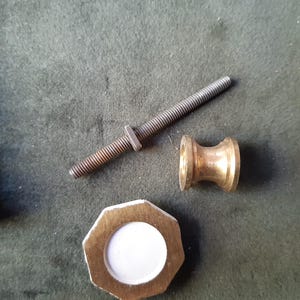 Peut inclure: Un ensemble de composants de quincaillerie comprenant une longue tige m&eacute;tallique filet&eacute;e, un petit connecteur en forme de bobine couleur laiton et une pi&egrave;ce octogonale plate couleur laiton avec un insert central circulaire blanc.