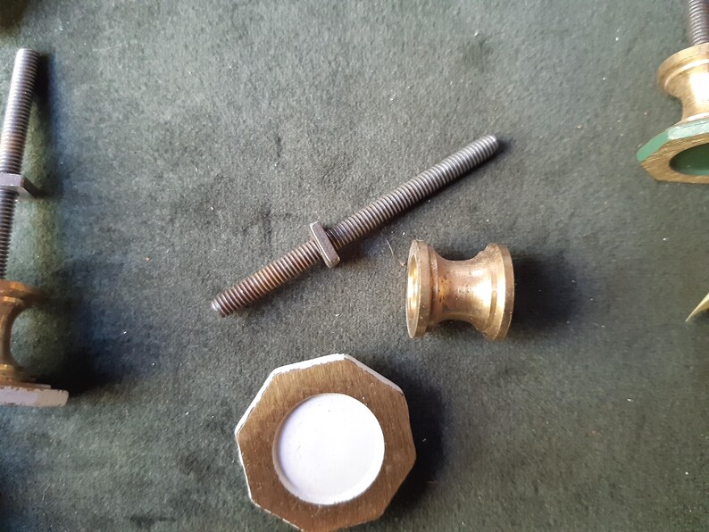 Peut inclure: Un ensemble de composants de quincaillerie comprenant une longue tige m&eacute;tallique filet&eacute;e, un petit connecteur en forme de bobine couleur laiton et une pi&egrave;ce octogonale plate couleur laiton avec un insert central circulaire blanc.