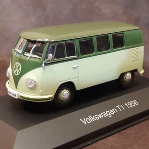 Peut inclure: Modèle réduit de Volkswagen T1 1956 vert et crème. Le bus miniature présente le logo VW à l'avant, des rétroviseurs latéraux et des roues noires. Le modèle est présenté sur une base noire avec le texte "Volkswagen T1 1956".