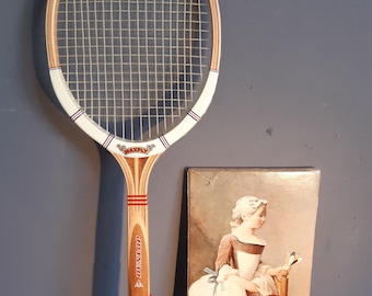 May include: A vintage Dunlop Maxply wooden tennis racket with a white frame, red and blue accents, and a brown leather grip, displayed alongside a rectangular box featuring a printed illustration of a person holding a similar wooden racket.