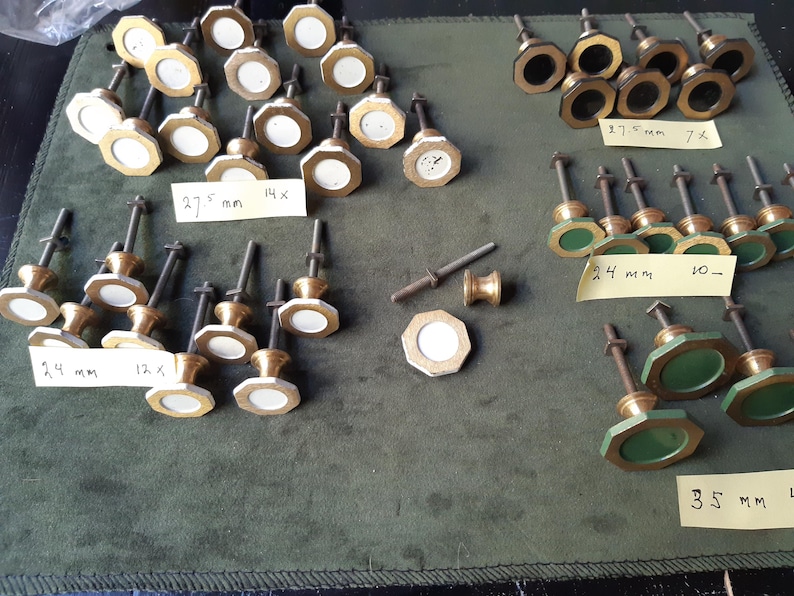 Peut inclure: Une collection de boutons de placard en m&eacute;tal avec des faces octogonales blanches, noires et vertes, organis&eacute;es par taille. Des &eacute;tiquettes indiquent des mesures de 27,5 mm, 24 mm et 35 mm. Chaque bouton poss&egrave;de une tige filet&eacute;e en m&eacute;tal.
