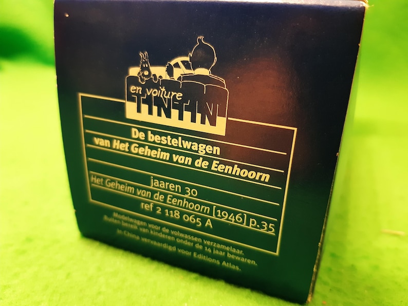 以下が含まれることがあります： ティンティンのロゴとオランダ語のテキストが特徴の濃い青色の箱。 箱には車に乗ったタンタンのイラストが含まれています。 テキストは「De bestelwagen van Het Geheim van de Eenhoorn」と「jaaren 30」と書かれています。