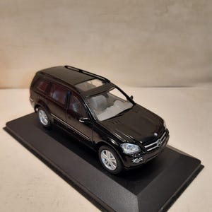 Pode incluir: Modelo preto de um SUV Mercedes-Benz em um suporte de exibição preto. O carro em miniatura tem rodas prateadas, teto solar e faróis detalhados. O modelo é uma réplica de um veículo de luxo.