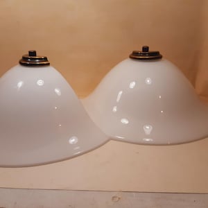 May include: Two white glass lampshades with a bell shape. Each shade has a brass-coloured cap on top. The shades are smooth and glossy, reflecting light. The design is simple and elegant, suitable for various interior styles.