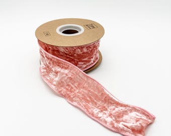 May include: A spool of pink velvet ribbon with a crinkled texture. The ribbon is unwound, revealing its soft, plush surface. The spool is made of cardboard.