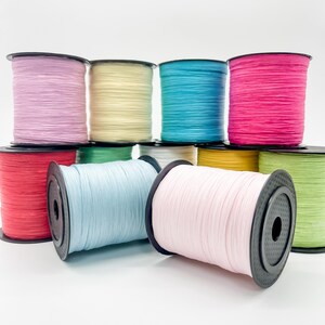 May include: A collection of eleven spools of raffia ribbon in various colors including light pink, pale yellow, bright turquoise, hot pink, red, light green, white, golden yellow, lime green, light blue, and soft pastel pink on black plastic reels.