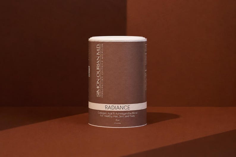 May include: A cylindrical brown container of Simon Ourian M.D. Radiance supplement powder. The label features white text reading Radiance, Collagen, Acai & Ashwagandha Blend For Healthy Hair, Skin, and Nails, and Personalized Lifestyle Nutrition.