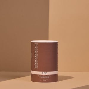 Può includere: Un contenitore cilindrico con un'etichetta marrone e un coperchio bianco. L'etichetta presenta il testo "RISE" e "Hyaluron & Guarana Mix For Daily Energy". Il prodotto è di Simon Ourian M.D. Personalized Lifestyle Nutrition.