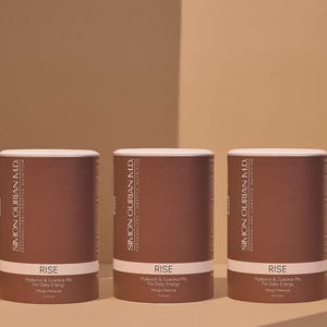 Può includere: Tre contenitori cilindrici marroni con coperchi bianchi. Ogni contenitore riporta la scritta "SIMON OURIAN M.D." e "RISE". I contenitori sono per l'energia quotidiana.