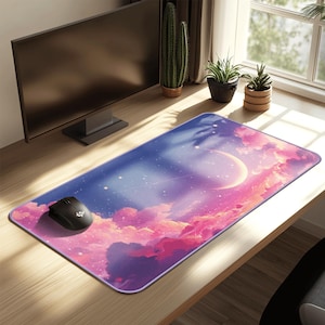 Op de afbeelding: Een rechthoekige bureaumat met een levendige hemelse print van een maansikkel, verspreide sterren en roze en paarse wolken. Een zwarte computermuis rust op de linkerkant van de mat, die een glad oppervlak en afgeronde hoeken heeft.