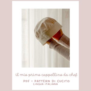 Può includere: Un cappello da chef beige è tenuto in alto da due mani. Il cappello è realizzato in un tessuto morbido e ha un bordo strutturato. Il testo in basso recita "il mio primo cappellino da chef" e "PDF • PATTERN DI CUCIOTTO LINGUA ITALIANA".